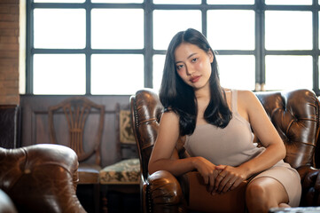 Young classy Asian woman sitting on vintage sofa in the luxury and fancy living room.