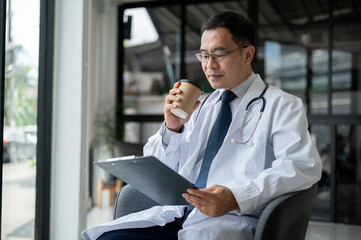 A professional male doctor is sipping coffee and reading and examining medical cases in his office