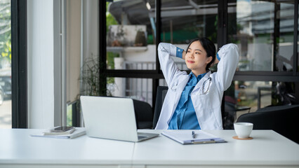 A carefree doctor is putting her hands behind her head, taking a break after work at her desk.