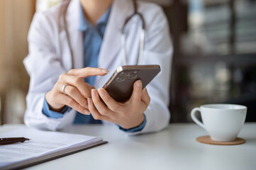 Fototapeta na wymiar A female doctor using her smartphone at her desk in the hospital office, responding to messages