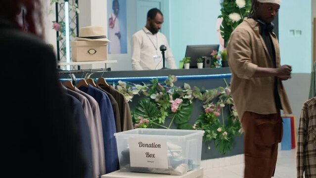 Customers donating stylish formal clothes in fancy fashion boutique, doing good deed. Generous clients adding their garments in donation box for charitable event organized by premium showroom