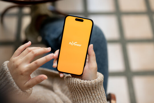 Close-up image of a woman using Payoneer application on her IPhone14 while sitting outdoors.