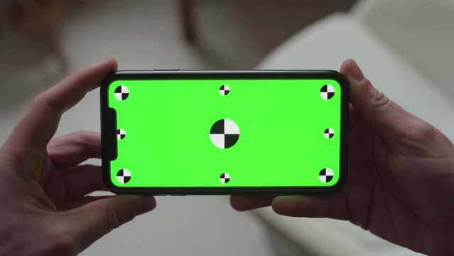 hands holding smartphone with green screen display and tracking markers, changing orientation from portrait to landscape and back to portrait again
