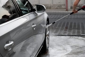 Washing luxury silver car on touchless car wash. Washing sedan car with foam self-service and high...