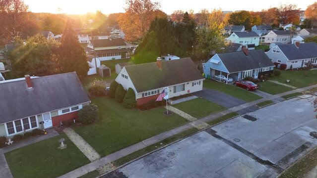 Suburban neighborhood with single-family homes and an American flag at sunset. Aerial shot during golden hour. Push in.