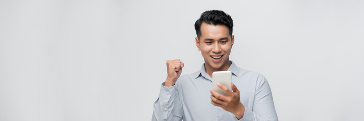 A happy young man holding mobile phone and celebrating success isolated over white background