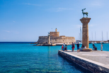 Naklejka premium Mandraki port with deers statue, where The Colossus was standing and fort of St. Nicholas. Rhodes, Greece. Hirschkuh statue in the place of the Colossus of Rhodes, Rhodes, Greece