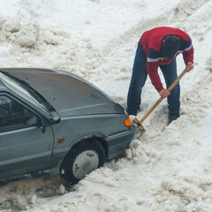 A man digs a shovel of snow from a car stuck in the snow