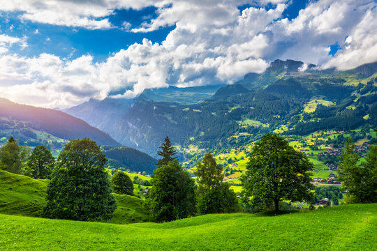 Grindelwald village view and summer Swiss Alps mountains panorama landscape, wooden chalets on green fields and high peaks in background, Switzerland, Bernese Oberland, Europe.