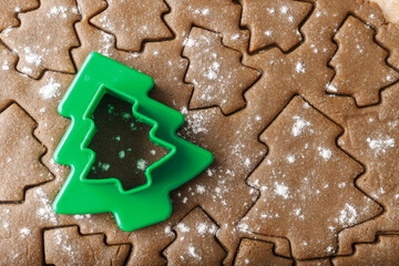 Cooking ginger cookies, Christmas New Year traditional cookies in shape of Christmas fir tree, raw rolled out dough with cut out dough figures, closeup, top view, green plastic pastry cutter on dough