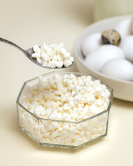 A spoon with cottage cheese close-up, cottage cheese with a glass bowl and a porcelain bowl with eggs. Dietary nutrition