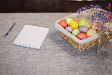 A notebook with a pen on the table and a basket with painted eggs for Easter