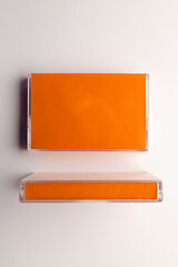 Overhead view of two orange cassette tape boxes arranged on white background