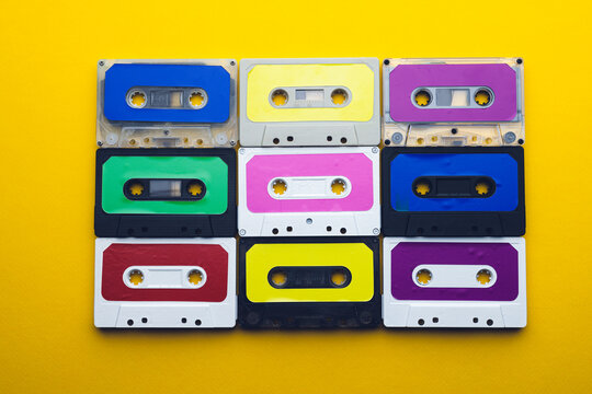 Overhead view of nine colourful cassette tapes arranged on yellow background