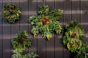 Snowflake shaped fresh Christmas wreath make out of evergreen branches, pinecones and red berries, hanging on a wood wall
