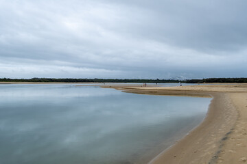 Cotton Tree at the mouth of the Maroochy River, Queensland, Australia. People fishing and walking around the beach on low tide. Reflection of cloudy sky in the water.