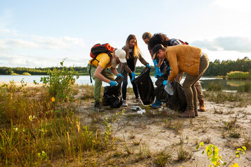 This image captures a group of individuals actively participating in a lakeside cleanup. Dressed in...