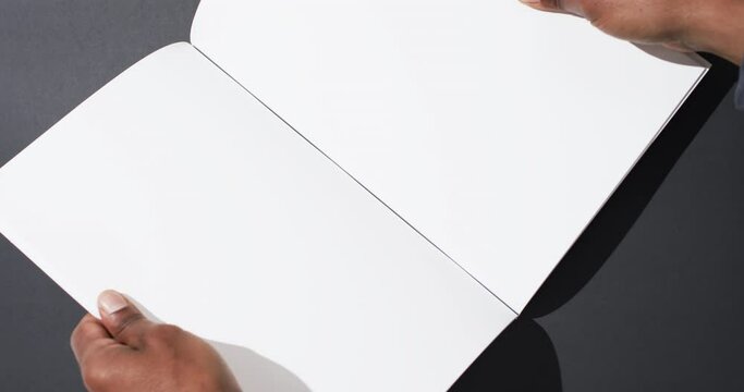 Video of hand of african american man holding book with blank pages, copy space on black background