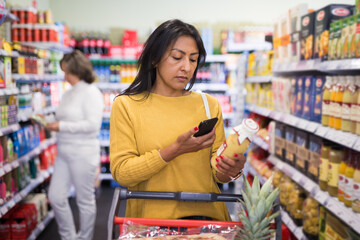 Latin american woman making purchases in grocery store, using smartphone to scan barcode of products. Modern shopping concept