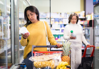 Portrait of interested latin american woman choosing fresh dairy products on refrigerated shelves...