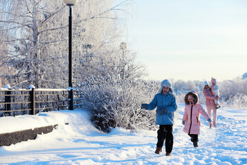 Family with children play snowy winter games in the park. Winter holidays and family vacation. Winter walk on the street on a sunny frosty day.
