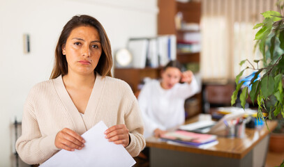 Portrait of young frustrated woman holding dismissal letter at office