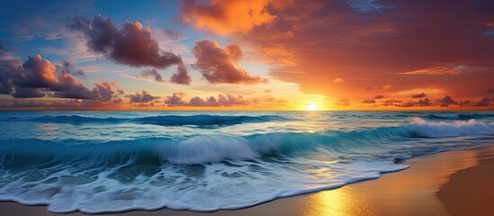 As the sun sets over the rippling ocean, casting a warm golden light upon the beach, the sky transforms into a breathtaking canvas of vibrant hues - a mesmerizing blend of blue, red, and orange. The - obrazy, fototapety, plakaty