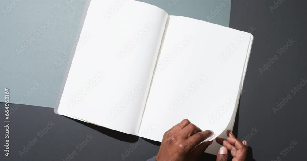 Wall mural Video of hand of african american man holding book with blank pages, copy space on black background