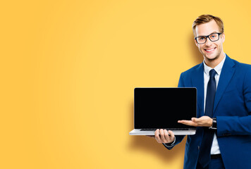 Smiling business man in glasses spectacles, suit show laptop with empty mockup screen, isolated against yellow background, copy space. It expert,  technician repair service, tech support maintenance