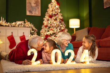 Grandchildren and grandparents holding illuminative numbers 2024 for New Year's Eve