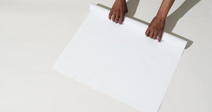 Video of hands of african american man with rolling up white paper on white background