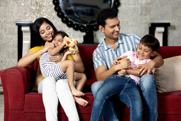 portrait of indian family together sitting on sofa in living room looking each other , Happy family having fun together