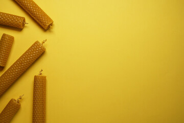 Stylish elegant beeswax candles, wax sheets on yellow background. Top view, flat lay. Space for text.