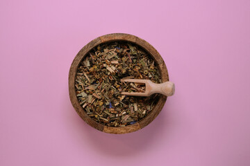 Wooden bowl with scoop and dry tea leaves on a pink background. Top view.