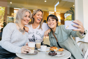 Happy adult friends taking selfie in cafe on weekend day