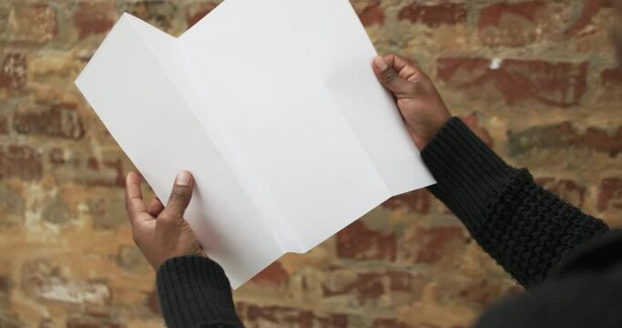 Video of hand of african american man holding white blank page, copy space over brick wall