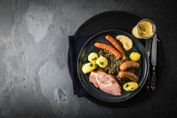 Oldenburger Grünkohl mit geräucherter Kohlwurst, Pinkel, Kassler Nacken, Kartoffeln, Senf, Petersilie auf Teller und dunkel schwarz Schiefer Hintergrund