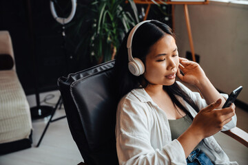 Woman listening music with headphones and smartphone while sitting on chair at home