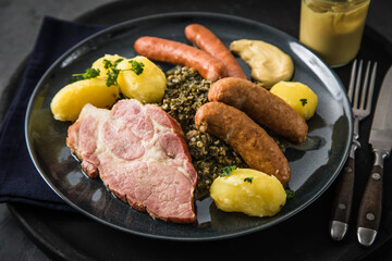 Oldenburger Grünkohl mit geräucherter Kohlwurst, Pinkel, Kassler Nacken, Kartoffeln, Senf, Petersilie auf Teller und dunkel schwarz Schiefer Hintergrund