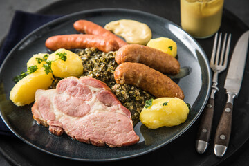 Oldenburger Grünkohl mit geräucherter Kohlwurst, Pinkel, Kassler Nacken, Kartoffeln, Senf, Petersilie auf Teller und dunkel schwarz Schiefer Hintergrund