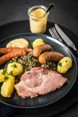 Oldenburger Grünkohl mit geräucherter Kohlwurst, Pinkel, Kassler Nacken, Kartoffeln, Senf, Petersilie auf Teller und dunkel schwarz Schiefer Hintergrund