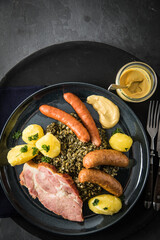 Oldenburger Grünkohl mit geräucherter Kohlwurst, Pinkel, Kassler Nacken, Kartoffeln, Senf, Petersilie auf Teller und dunkel schwarz Schiefer Hintergrund