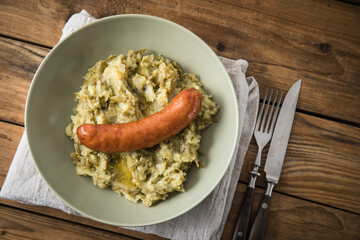 Schnibbelbohnen Eintopf aus fermentierten Stangenbohnen und Kartoffeln mit Mettwurst und zerlassener Butter auf grün Teller mit Besteck, Leinen Serviette und rustikalen Holz Hintergrund