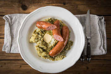 Schnibbelbohnen Eintopf aus fermentierten Stangenbohnen und Kartoffeln mit Mettwurst und zerlassener Butter auf Teller mit Besteck, Leinen Serviette und rustikalen Holz Hintergrund
