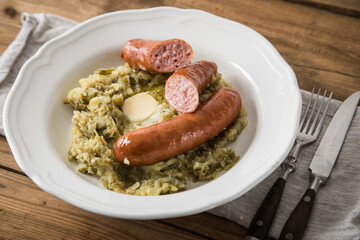 Schnibbelbohnen Eintopf aus fermentierten Stangenbohnen und Kartoffeln mit Mettwurst und zerlassener Butter auf Teller mit Besteck, Leinen Serviette und rustikalen Holz Hintergrund