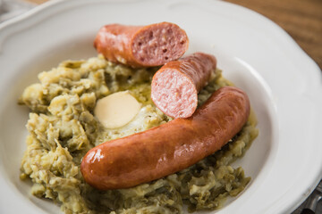 Schnibbelbohnen Eintopf aus fermentierten Stangenbohnen und Kartoffeln mit Mettwurst und zerlassener Butter auf Teller mit Besteck, Leinen Serviette und rustikalen Holz Hintergrund