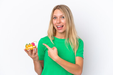Young caucasian woman holding a tartlet isolated on white background pointing back