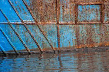 Rusty structure on a blue abandoned ship hull in a harbor