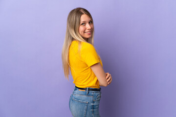 Young blonde woman isolated on purple background looking to the side and smiling