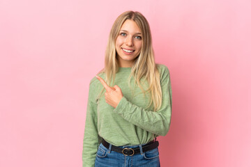 Young blonde woman isolated on pink background pointing to the side to present a product